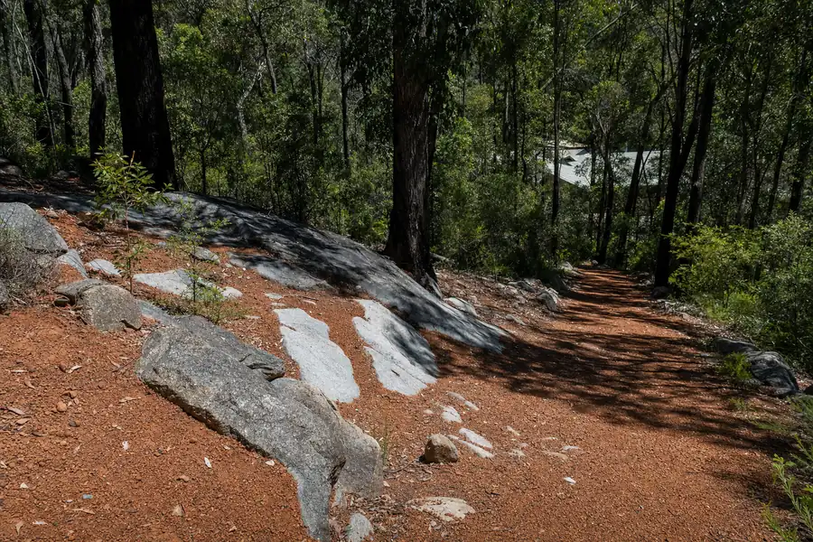 A steep Perth Hills block of orange-red lateritic gravel with exposed grey granite outcrop, jarrah and marri forest running to the boundary — illustrative example